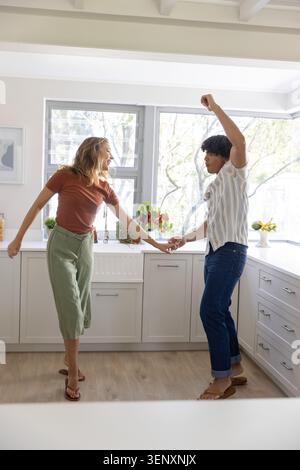 Couple holding hands and dancing in sunlit kitchen in casual outfits by farmhouse sink Stock Photo