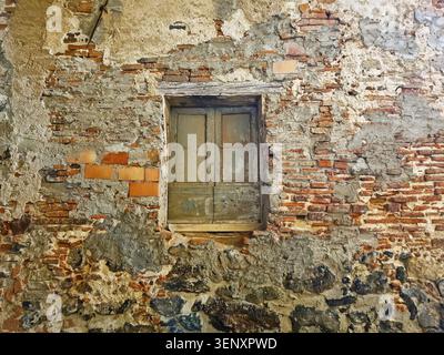 A boarded-up wooden window in the weathered brick wall of an abandoned house Stock Photo