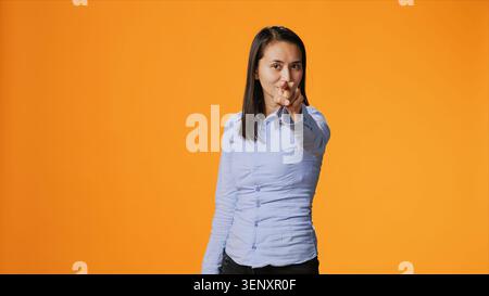 Model pointing at the camera in colorful studio, looking into the lens with confidence, with young filipino woman points index finger and standing proud against orange background. Stock Photo