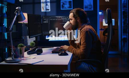Focused programmer drinking coffee in apartment while solving database errors on computer, remotely working IT admin concentrated on finalizing coding project in home office. Stock Photo