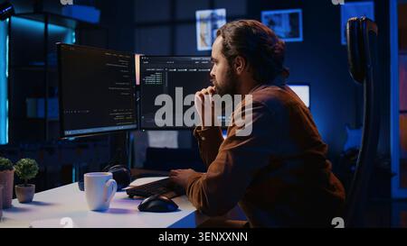Programmer doing web development during remote job shift in neon lit home office, finishing coding project, IT specialist sitting at computer desk, working on desktop PC. Stock Photo