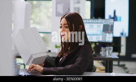 Developer analyzing 3D building model at realty office, examining measurements for the actual construction scale, engineer calculating industrial lines and elements on laptop blueprint draft. Stock Photo