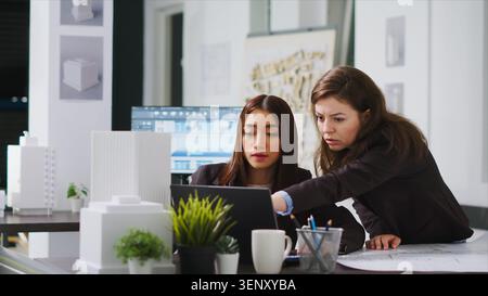 Industrial engineers designing floor plan sketch on CAD software, using laptop to determine measurements of apartment for remodeling projects, architects working at unicorn business office. Stock Photo