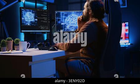 Freelancing programmer writes code on desktop PC to visualize artificial intelligence neural networks, self employed man runs AI script on computer from apartment office, jib down shot. Stock Photo