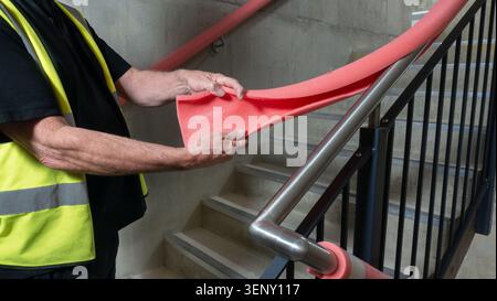 Quality control surveyor inspecting handrail guard covers on an industrial stairwell.  Construction engineer removing foam handrail covers at the end Stock Photo