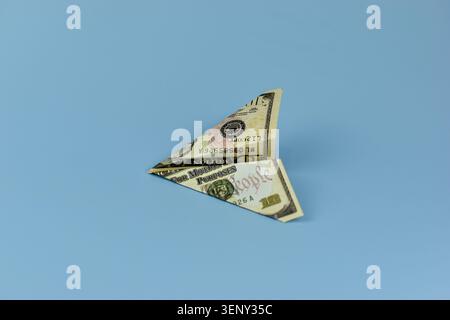 Folded dollar bill creates a delicate butterfly shape. Its wings mimic flight, as if ready to soar. Soft blue background enhances its artistic simplic Stock Photo