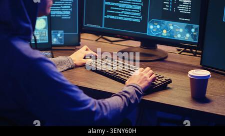 Young hacker drinking coffee while running spyware software designed to gather information from users computers without their knowledge, script kiddie doing illegal stuff in graffiti painted hideout. Stock Photo