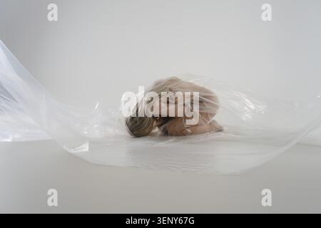 A blonde woman in a studio poses with transparent material, exuding serenity and beauty Stock Photo