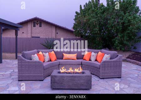 Outdoor circular wicker patio set sectional with throw pillows and a fire table at dusk Stock Photo