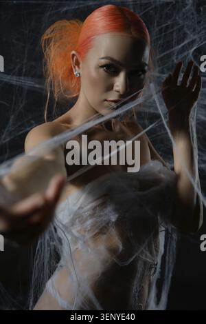A striking red-haired woman is ensnared in a web, blending beauty and tension in a captivating scene Stock Photo