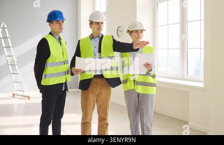 Contractors discussing blueprints during interior renovation inspection on site Stock Photo