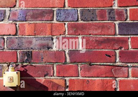 Retro wall-mounted light switch with exposed wiring on an aged red brick wall, creating an industrial and abandoned urban aesthetic. Brickwork. Stock Photo