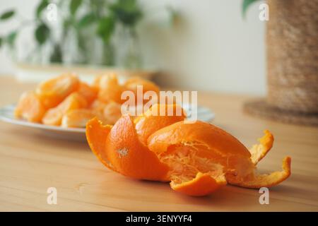 Peeled orange sits on table with more oranges in background Stock Photo