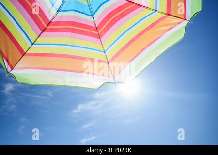 Colorful striped beach umbrella against bright blue sky with sun flare, summer vacation and relaxation Stock Photo