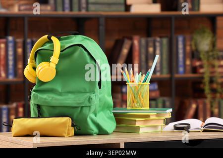 Green school backpack with yellow headphones and pencil case on desk, education and learning supplies Stock Photo