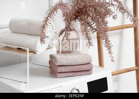Freshly laundered white and pink towels on washing machine with decorative plant in modern bathroom, sense of domestic comfort and meticulous home car Stock Photo