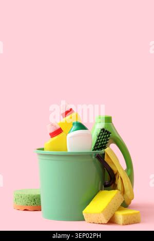Household cleaning supplies in green bucket with sponges and gloves on pink background, sponges are placed beside the bucket, all set against a solid Stock Photo
