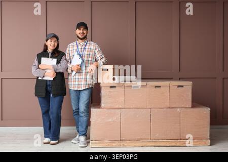 Smiling delivery team with clipboards and stacked cardboard boxes for moving or logistics services, the male and female workers are dressed in casual Stock Photo