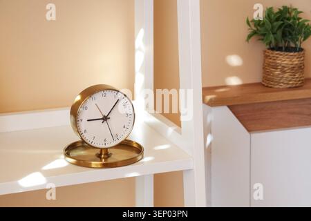 Modern brass desk clock on white shelf with plant, time management and home decor Stock Photo