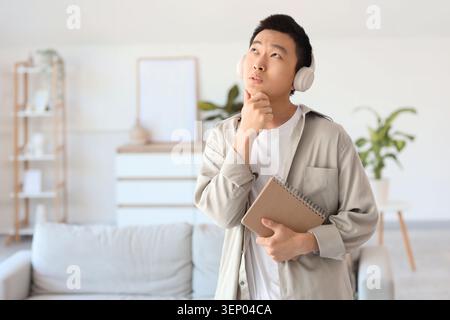 Thoughtful young Asian man with notebook and headphones at home Stock Photo
