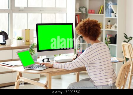 Young woman working remotely with green screen desktop computer and laptop in modern home office environment Stock Photo