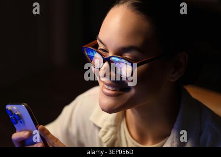 Smiling woman wearing glasses with data reflections using smartphone in dark room digital information and technology, the image concepts of technology Stock Photo