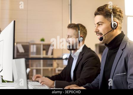 Two call center agents with headsets at office computers, providing support Stock Photo