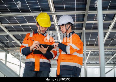 Young technician and Engineer examine solar panels. Both in orange safety jackets with stripes. Check power consumption received via tablet together, Stock Photo