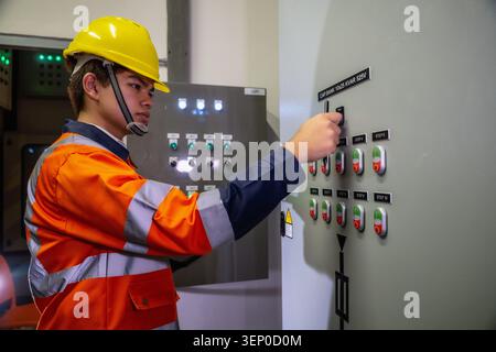 Asian industrial worker turning switch on industrial control panel switchboard, checks control panel inside industrial control room. Control panel has Stock Photo