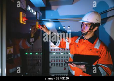 Young electrical engineer holding tablet operating main isolator switch panel, turning disconnector switch power station in control room Stock Photo