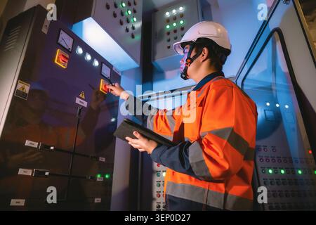 Professional engineer in high visibility jacket controlling electricity cabinet, holding tablet operating main power supply switch, operating breaker Stock Photo