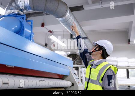 Factory engineer pointing finger inspecting industrial ventilation duct system, checking HVAC airflow pipe factory machinery, wearing safety vest look Stock Photo