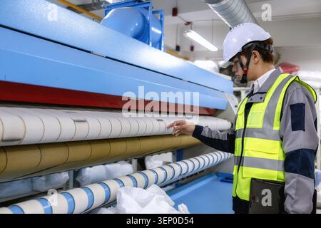 Factory engineer inspecting industrial flatwork ironer roller machinery, pointing at roller system and adjusting settings on large industrial pressing Stock Photo