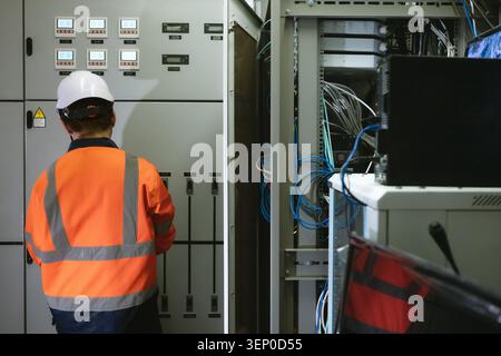 Asian young electrical engineer recording operation metrics on digital tablet screen indoor in control room, An electrical technician in a bright oran Stock Photo
