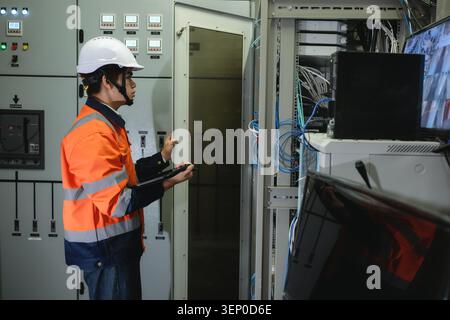 Asian young IT engineer in uniform using tablet and open to server rack cabinet, Systems engineer in safety gear examines server equipment, Configurin Stock Photo