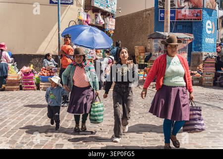 Cusco, Peru - March 23, 2025: Local indigenous women dressed in traditional Andean attire walk along the cobblestone street carrying market bags outsi Stock Photo