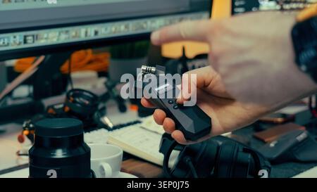 Creator hand holding portable audio field recorder adjusting settings studio workstation monitor. Close up view of a sound designer adjusting paramete Stock Photo