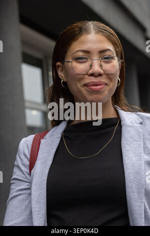 African American woman standing outside concrete building wearing gray blazer and glasses Stock Photo