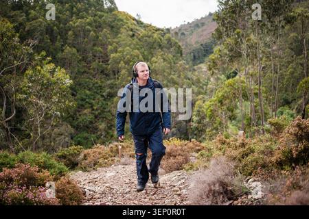 Man with backpack and headphones walking uphill on a rocky path through nature Stock Photo