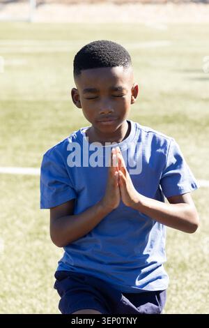 African American schoolboy praying with hands pressed to chest on artificial turf with white lines Stock Photo