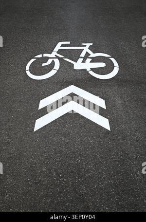 Bicycle lane road marking painted on asphalt with directional arrows. Urban cycling infrastructure symbol indicating bike path direction. Stock Photo