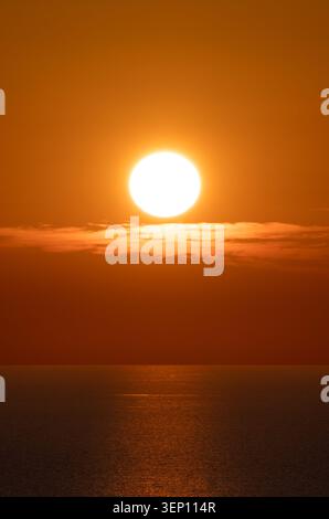 Close-up of a large, radiant sunset illuminating low clouds over the Mediterranean Sea from the Cavalleria lighthouse viewpoint in Menorca, Spain. Stock Photo
