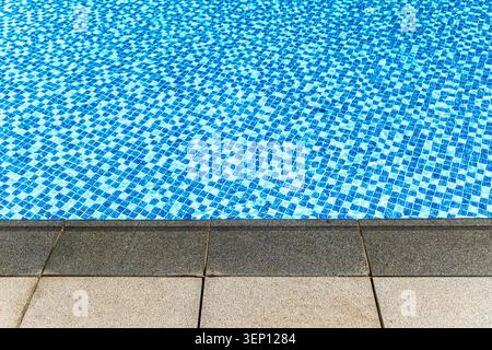 Close-up view of a blue mosaic tile swimming pool surface with a gray stone border, showcasing the vibrant colors and textures of the tiles Stock Photo