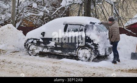 Man scraping snow from car in harsh winter conditions during a blizzard Stock Photo