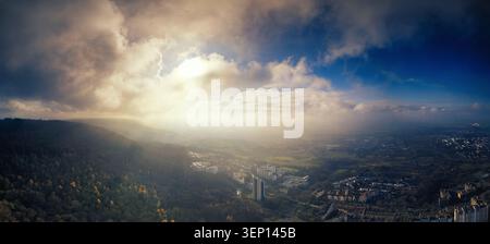 Aerial panorama view of dramatic illuminated clouds and the setting sun over a town and hills Stock Photo