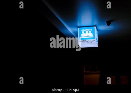 Blue light glows softly on a square sign. Two stylized figures stand beneath the illumination. The sign shows clear, bold text against a white background Stock Photo