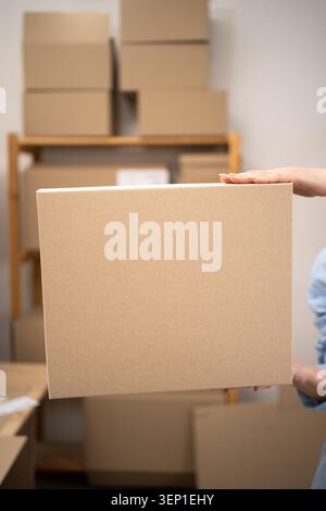 Female logistics worker holding cardboard boxes in warehouse. Woman taking box for parcel delivery and cargo distribution. mock up, close-up Stock Photo