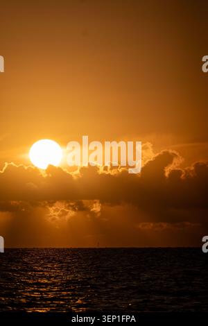 Dramatic Sunset with Large Glowing Sun Breaking Through Dark Storm Clouds Over the North Sea Stock Photo