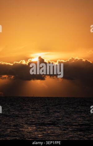 Dramatic Sunset with Sun Hidden Behind Dark Cloud Bank and Golden Light Rays Over the North Sea Stock Photo