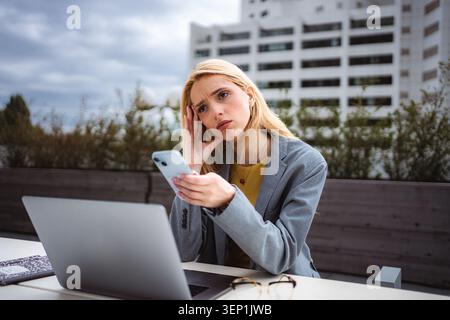 Stressed young woman working remotely outdoors using smartphone Stock Photo
